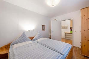 Une chambre à coucher comprenant un lit, une tête de lit en bois, une table de chevet, une commode, une lampe fixée au mur, une porte et un miroir.
