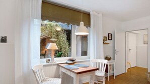 Ein Zimmer mit Esstisch, zwei Stühlen, einem Fenster mit Vorhängen, einer Pendelleuchte und einer Tür.