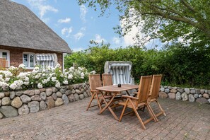 A brick house with a thatched roof, a stone wall, and a patio with a wooden table and chairs.