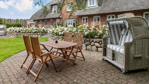 A patio with a table and chairs, a wicker sofa, and a brick house with a thatched roof. - Apartment 'Fewo Luna' with Private Terrace, Shared Garden and Wi-Fi (Emmelsbüll-Horsbüll)