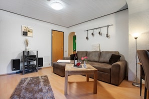 A living room with a sofa, a coffee table, a TV stand, and a lamp. - Apartment 'Rosi's Ferienwohnung' with Private Garden and Wi-Fi (Hohenzieritz)