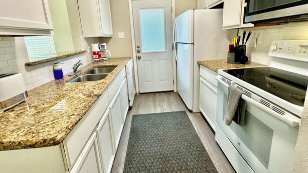 A kitchen with granite countertops, white cabinets, a refrigerator, a stove, and a microwave.