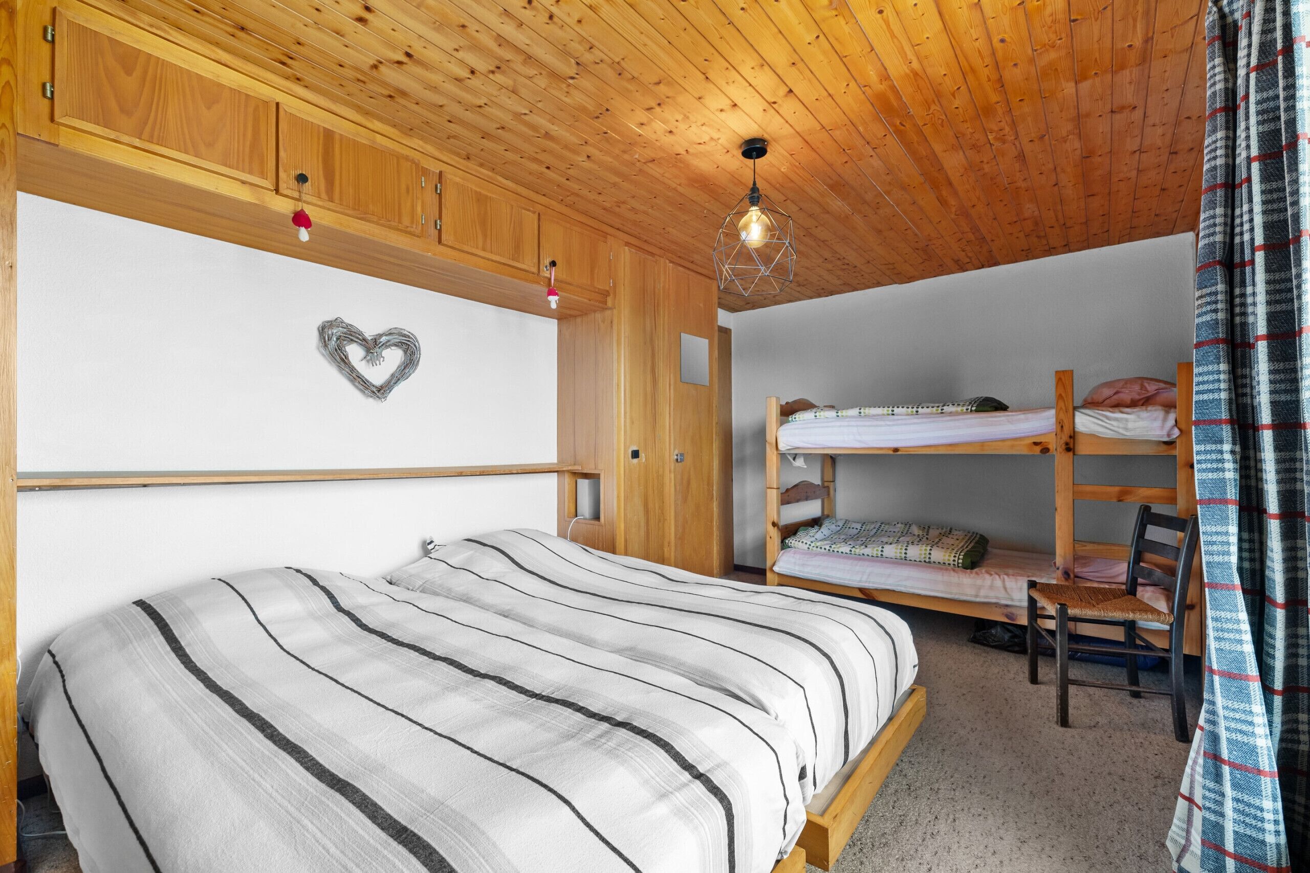 Une pièce comprenant un lit superposé, un lit simple, des armoires en bois et un luminaire suspendu.