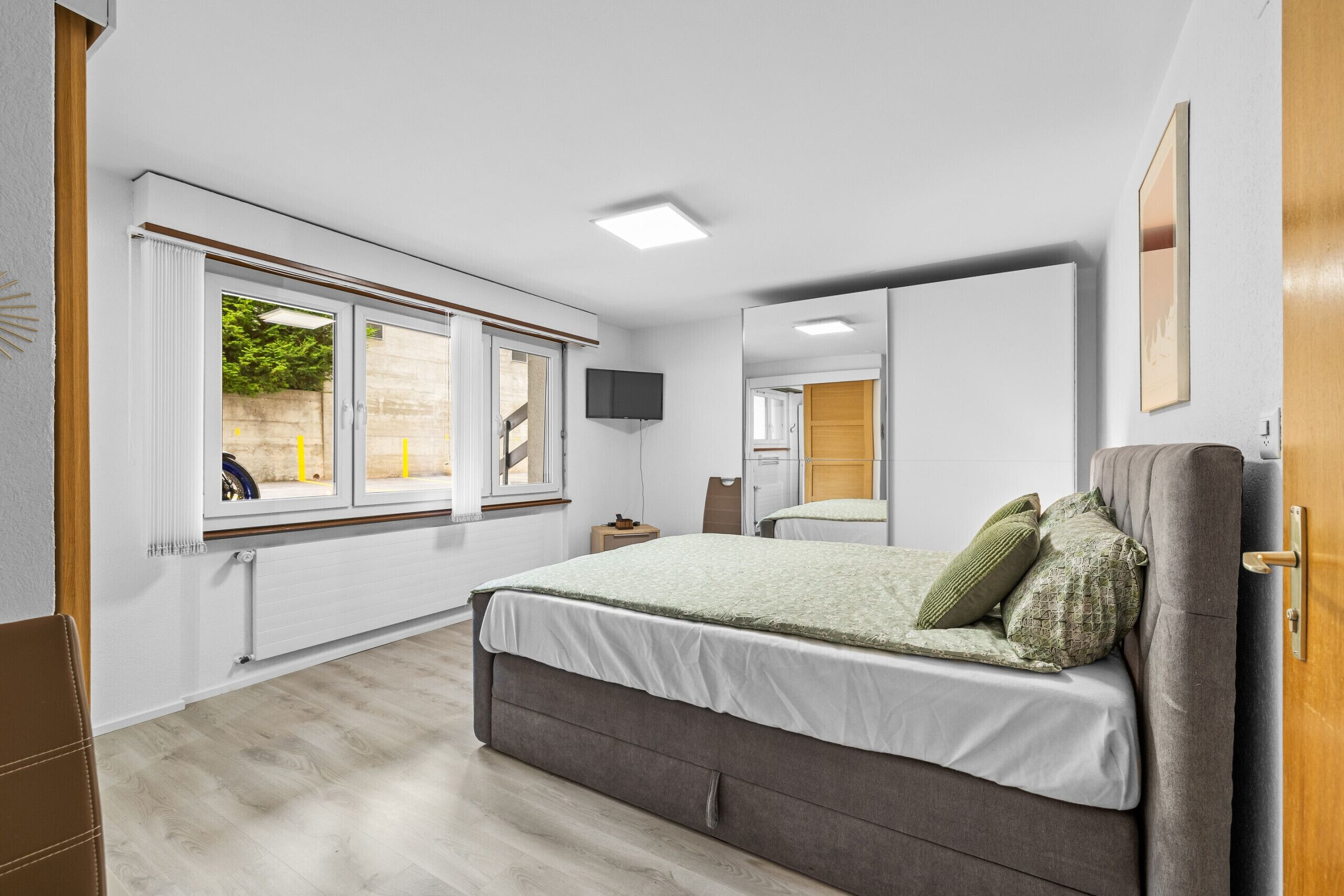 A bedroom with a bed, a window, a television, and a mirror.