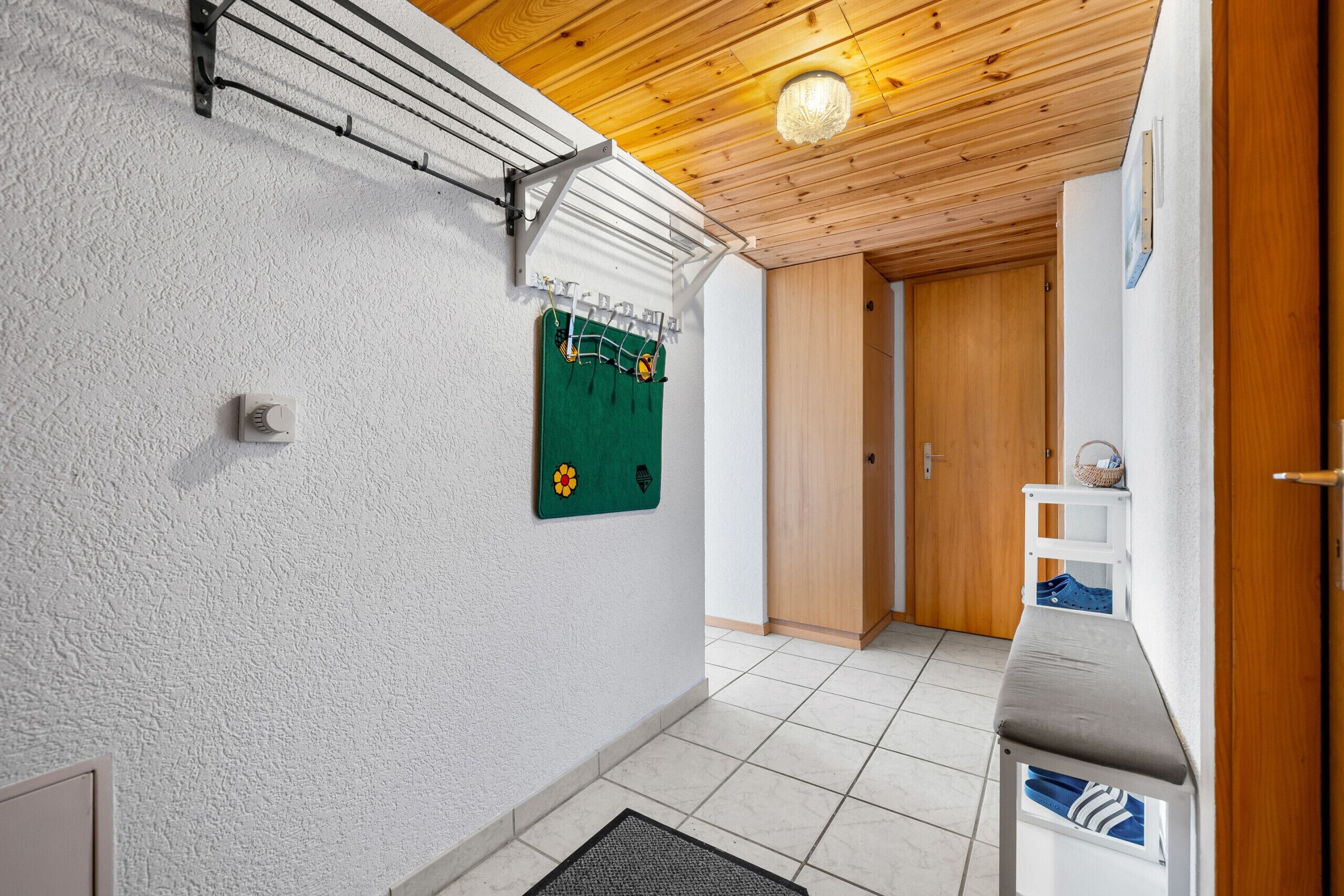 A hallway with a drying rack, a green towel with a logo, a wooden door, and a bench with a towel.