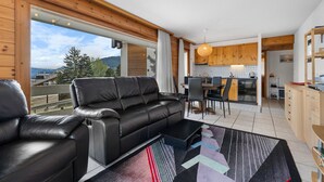 A modern living room with a black leather sofa, a dining area with a wooden table and chairs, and a kitchen with wooden cabinets and a hanging light fixture. - Les Hauts-de-Nendaz A A0 - 5 pers - ski In&Out (Haute-Nendaz)