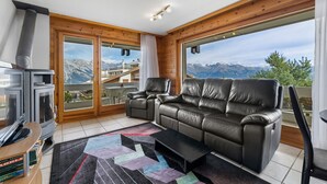 A living room with a fireplace, leather sofa, and a view of mountains. - Les Hauts-de-Nendaz A A0 - 5 pers - ski In&Out (Haute-Nendaz)