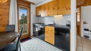 A compact kitchen with wooden cabinets, a black countertop, and a view through the door. - Les Hauts-de-Nendaz A A0 - 5 pers - ski In&Out (Haute-Nendaz)