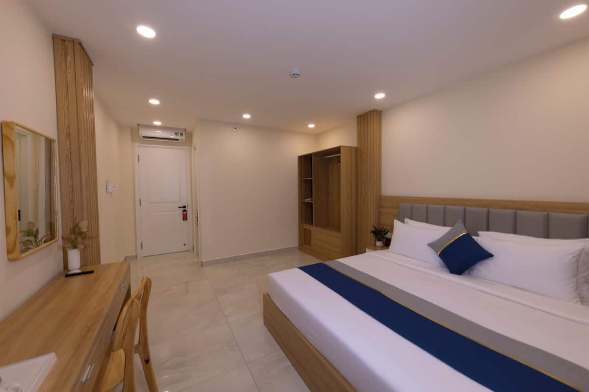 Une chambre d’hôtel moderne avec un grand lit, une armoire en bois, un bureau avec une chaise et un miroir.
