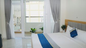 A hotel room with a bed, curtains, a potted plant, and a view through a glass door. - Ben Thanh Luxury Suite Hotel & Spa (Ho Chi Minh City)