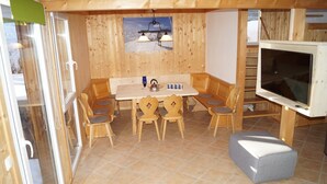 A wooden interior with a dining table, chairs, a TV, and a ski-themed picture on the wall. - Dreamy chalet on the slopes (Sankt Georgen am Kresichberg)