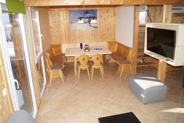 Interior de madeira com uma mesa de jantar, cadeiras, uma televisão e um quadro decorado com tema de esqui.