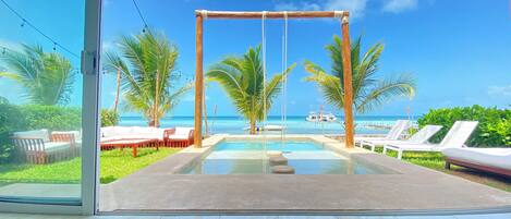 A pool area with lounge chairs and a view of the ocean.