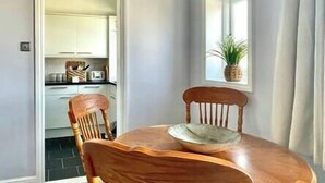A dining area with a round wooden table and two wooden chairs. A window with a plant on the windowsill is visible. - Perfectly Coastal, Quiet Central Retreat mins to Town Centre, Beach, Pier, Old Town & Train Station (Hastings)