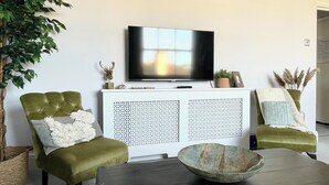 A living room with a television on a white cabinet, two green armchairs, a dark coffee table, and decorative items. - Perfectly Coastal, Quiet Central Retreat mins to Town Centre, Beach, Pier, Old Town & Train Station (Hastings)