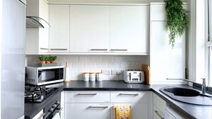 A modern kitchen with white cabinets, a black countertop, a microwave, a toaster, and a hanging plant. - Perfectly Coastal, Quiet Central Retreat mins to Town Centre, Beach, Pier, Old Town & Train Station (Hastings)