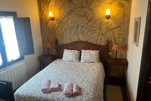 A hotel room with a bed, two bedside lamps, a window, and a radiator.