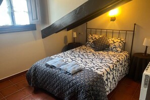 Un dormitorio con cama, mesita de noche, lámpara, ventana y calentador.