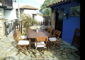 An outdoor patio with a wooden table and chairs, surrounded by stone flooring and a blue wall.
