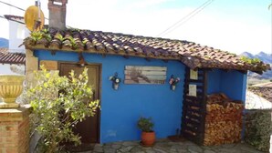 A blue building with a tiled roof, a stone-paved entrance, and a potted plant. - 15A08 El Rosal (Llanes)