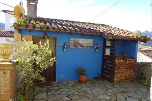 A blue building with a tiled roof, a stone-paved entrance, and a potted plant. - 15A08 El Rosal (Llanes)