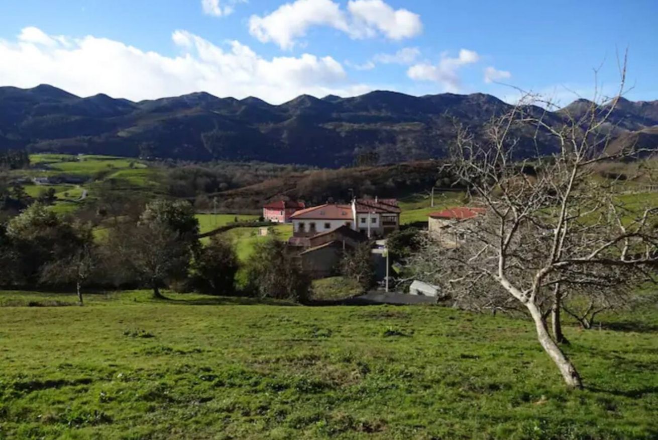 Un paisaje rural con una casa rodeada de campos verdes y montañas al fondo.