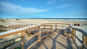 Un paseo marítimo de madera que conduce a una playa de arena, bajo un cielo despejado.
