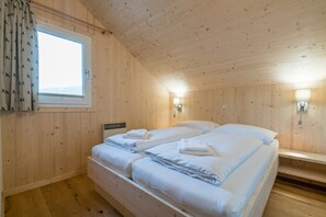 Un dormitorio de cabaña de madera con dos camas, una ventana con cortinas y luces fijadas a la pared.