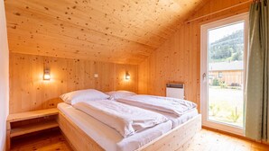 A wooden cabin bedroom with two beds, a window with a view of a forest, and wall-mounted lights. - Lavish Chalet in Sankt Georgen with Jacuzzi (Sankt Georgen am Kresichberg)