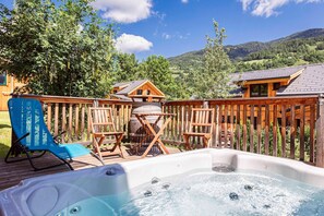 Eine Holzterrasse mit Whirlpool, Sitzgelegenheit und Blick auf eine Berglandschaft.