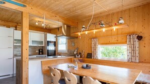 A wooden cabin interior with a kitchen, dining area, and a large window.