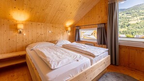 Un dormitorio de cabaña de madera con dos camas, una ventana con cortinas y vista a un paisaje boscoso.