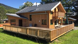 A wooden cabin with a balcony, a covered deck, and a chimney.