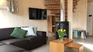 A modern living room with a black sofa, wooden coffee table, and a flat-screen TV mounted on the wall. - Appealing chalet in the ski area (Sankt Georgen am Kresichberg)