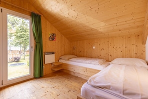Una habitación de cabaña de madera con una cama, una ventana con cortinas y una pequeña estantería.