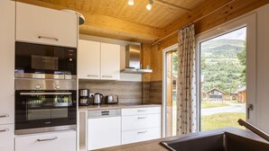 A modern kitchen with stainless steel appliances, white cabinetry, and a view of a mountainous landscape through a large window. - Appealing chalet in the ski area (Sankt Georgen am Kresichberg)