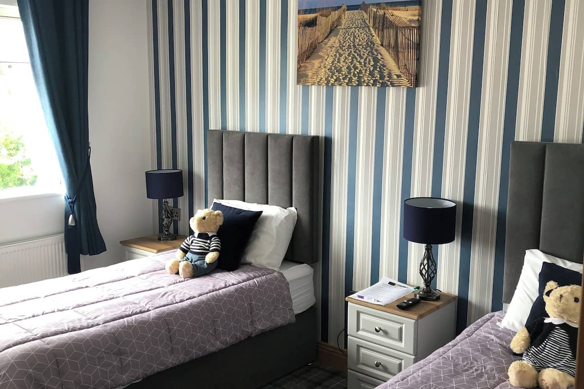 A hotel room with two beds, striped wallpaper, a painting, and a window with curtains.