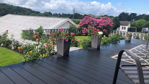 A deck with a view of a garden, a greenhouse, and a white building with a sloped roof. - Seacrest B&B (Galway)