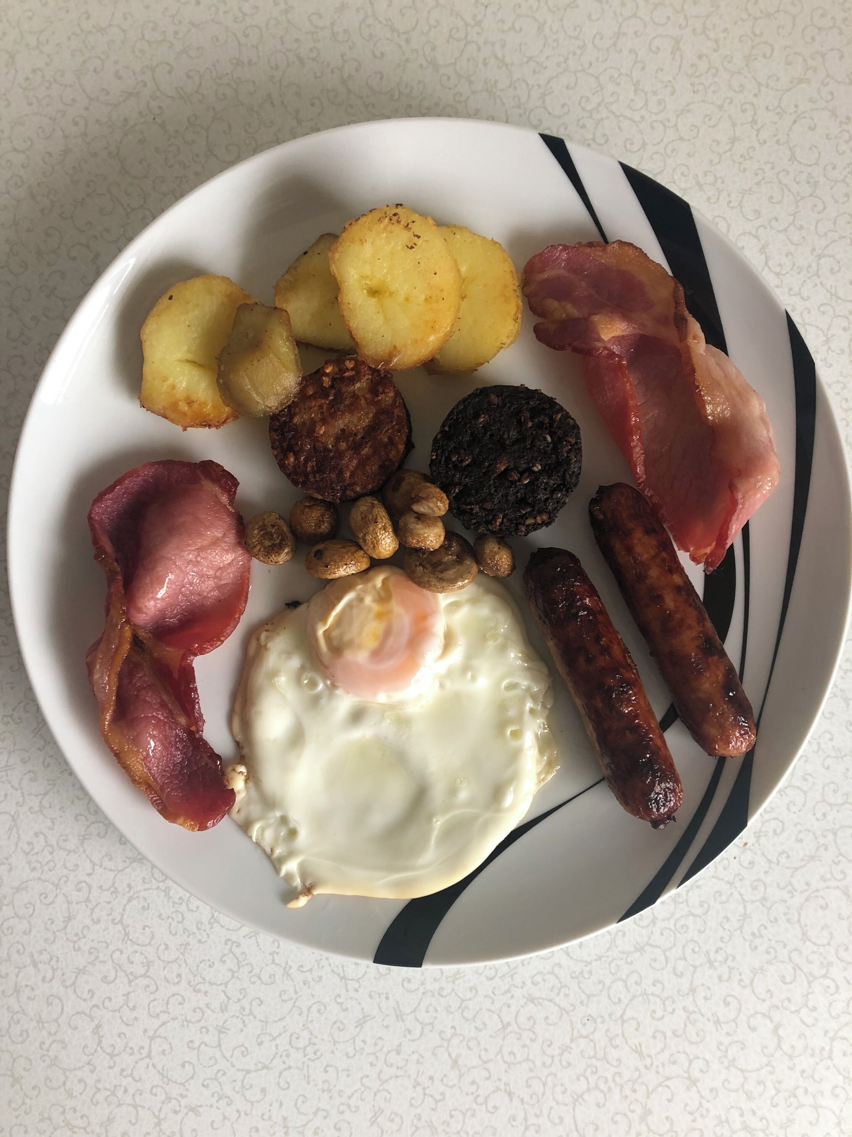Un plato con diversos alimentos para el desayuno, como huevos, salchichas, tocino y papas.
