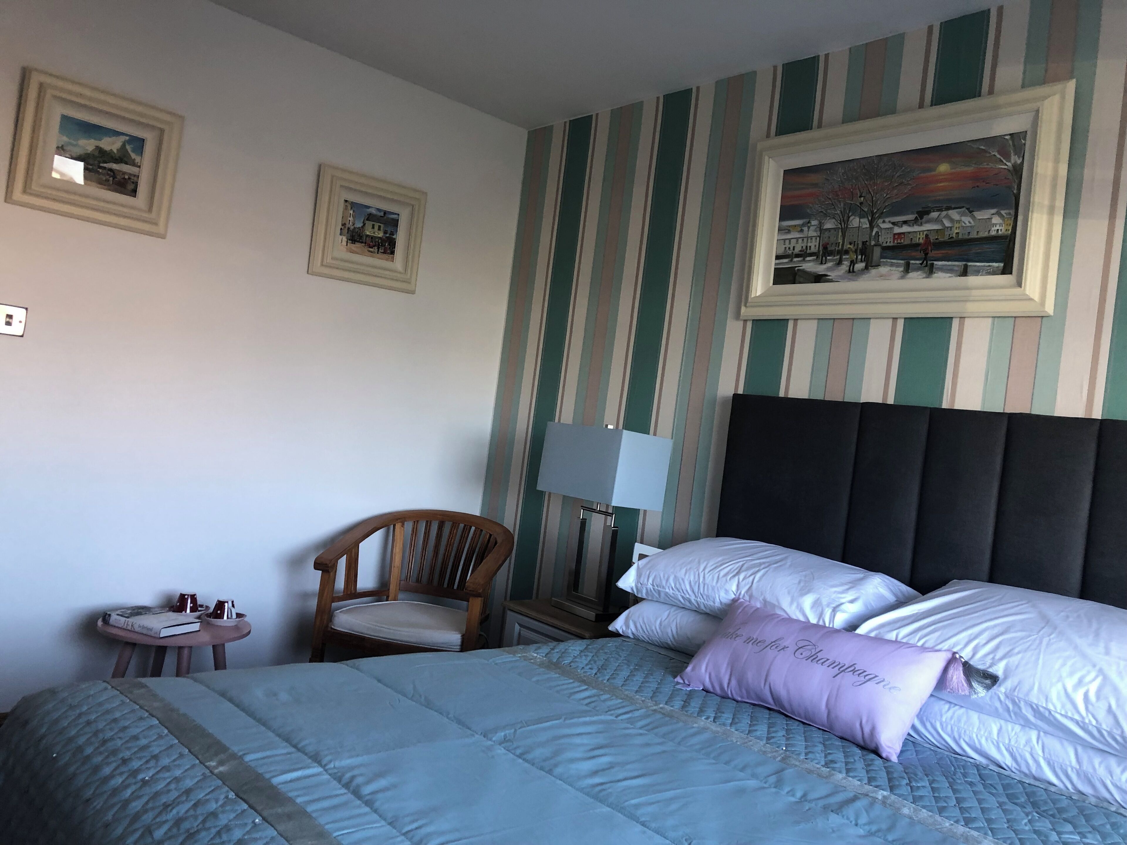 Ett hotellrum med en säng, en stol, ett nattduksbord och två inramade tavlor på väggen.