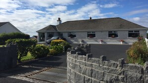 A two-story house with a stone wall and a car parked in the driveway. - Seacrest B&B (Galway)