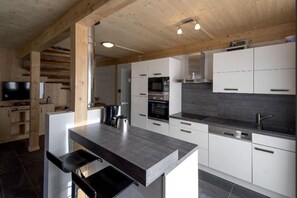 A modern kitchen with white cabinets, a dark countertop, and a wooden ceiling.