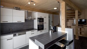A modern kitchen with white cabinets, a dark countertop, and a wooden ceiling.
