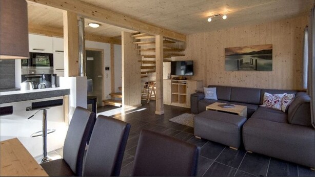 A modern interior with a kitchen, dining area, and living room. There is a staircase leading to an upper level.