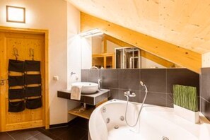 Un baño moderno con bañera, lavabo y ducha. Hay una puerta de madera con un perchero y una escalera que sube a un nivel superior.