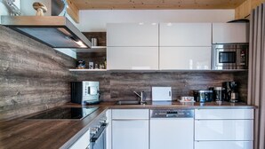 A modern kitchen with white cabinets, a built-in oven, a microwave, and a coffee machine.