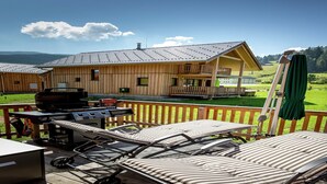 A wooden cabin with a deck, outdoor grill, lounge chairs, and a view of the surrounding landscape.