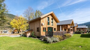 A wooden cabin-style building with a porch, surrounded by a grassy yard and trees.