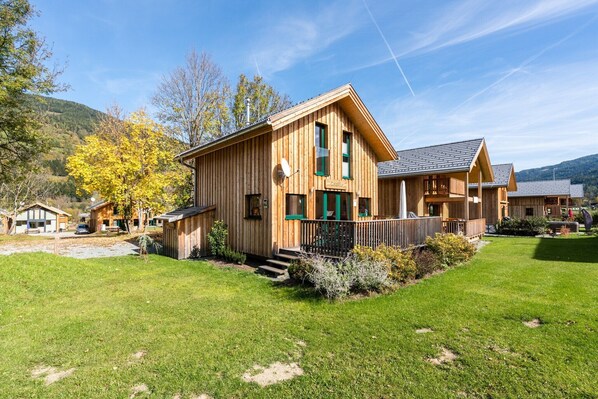 A wooden cabin-style building with a porch, surrounded by a grassy yard and trees.
