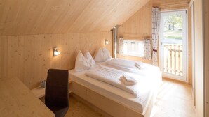 A wooden cabin bedroom with a large bed, a small desk, and a window with curtains.